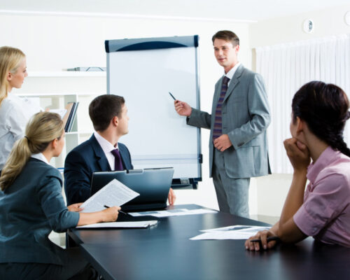 Image of smart business people looking at their leader while he explaining something on whiteboard during seminar
