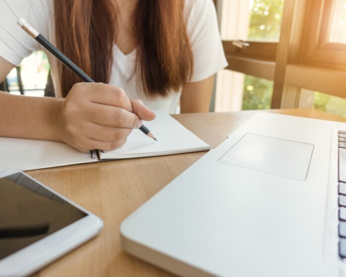 Female student taking notes from a book at library. Young asian